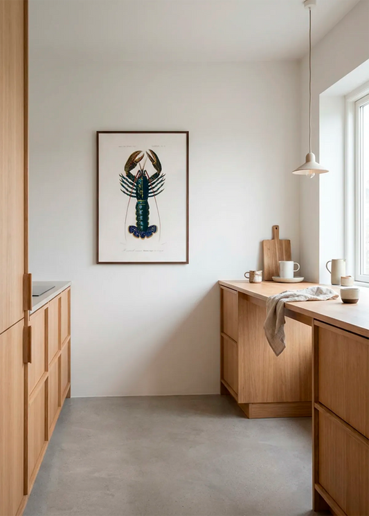 Indrammet hummerplakat hængt i et lyst, minimalistisk køkken med træfronter og nordisk indretning.