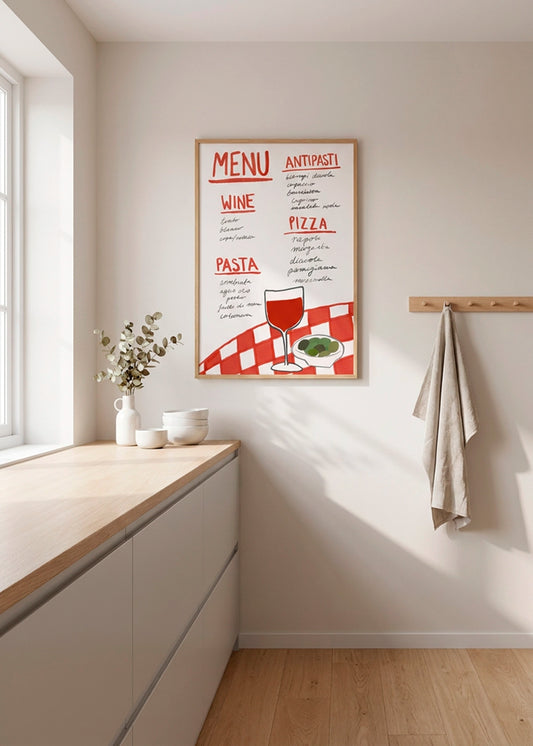 Indrammet menuplakat med vin, pizza, pasta og antipasti, hængt i et lyst nordisk køkken med trædetaljer og naturligt dagslys.