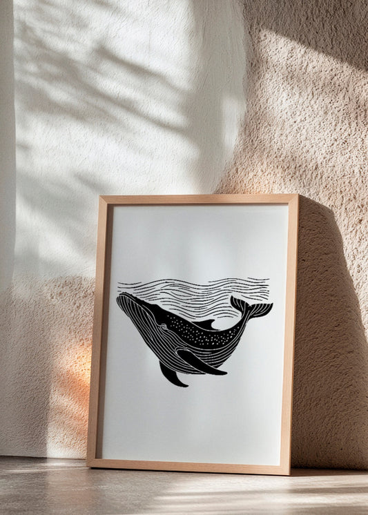 'Whale' poster in minimalist black and white, depicting a whale swimming under stylized waves. Framed in oak and leaning against a textured wall.