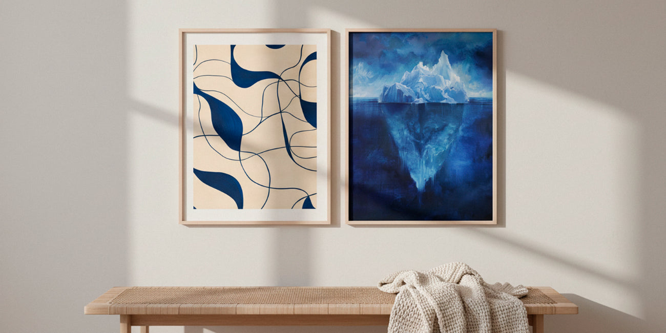 Iceberg Night and abstract blue line poster displayed side by side in oak frames above a minimal wooden bench, lit by soft natural daylight for a calm Scandinavian look.