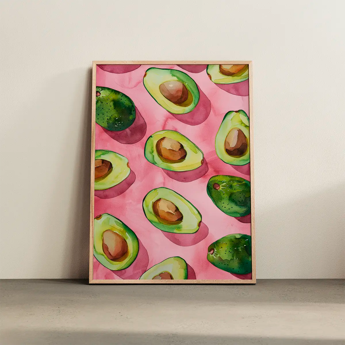Avocado poster with bright green watercolor avocados on a pink background, displayed in a light oak frame against a neutral wall.
