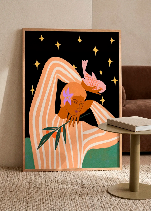 Balance by Arty Guava art print featuring a woman in a striped peach outfit with a pink bird, olive branch and golden stars, displayed in a light wood frame in a warm Scandinavian living room.