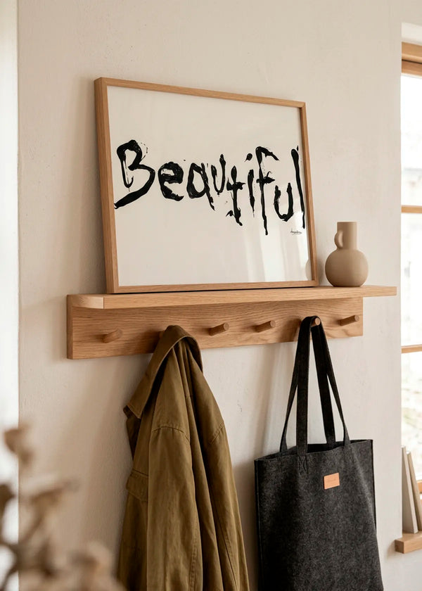 Beautiful Ink Script by Manasseh Johnson Sr. – framed black handwritten art poster with the word Beautiful on an off-white background, styled on a natural wood shelf in a warm neutral hallway.