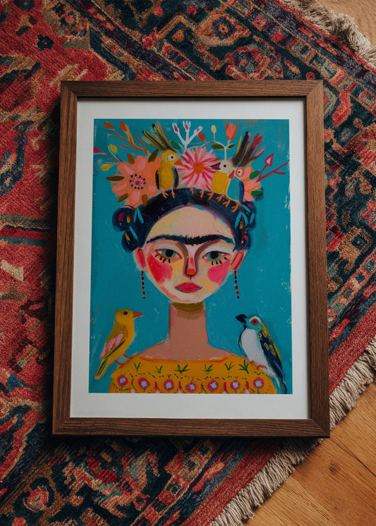 Colorful Frida Kahlo-inspired art print with birds and flowers in a wooden frame, styled on a patterned rug for a bohemian interior look.