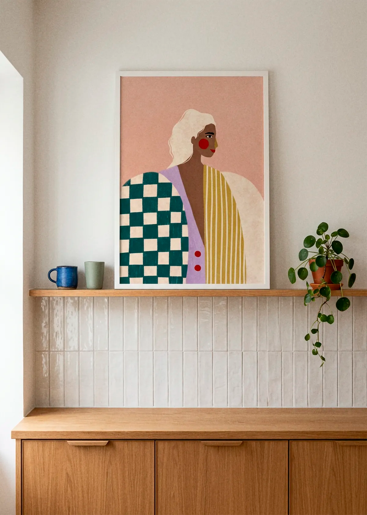 Bold Fashion Portrait by Bea Müller displayed in a white frame above warm oak kitchen cabinetry, styled with ceramic cups, glossy white tiles and a soft neutral wall.