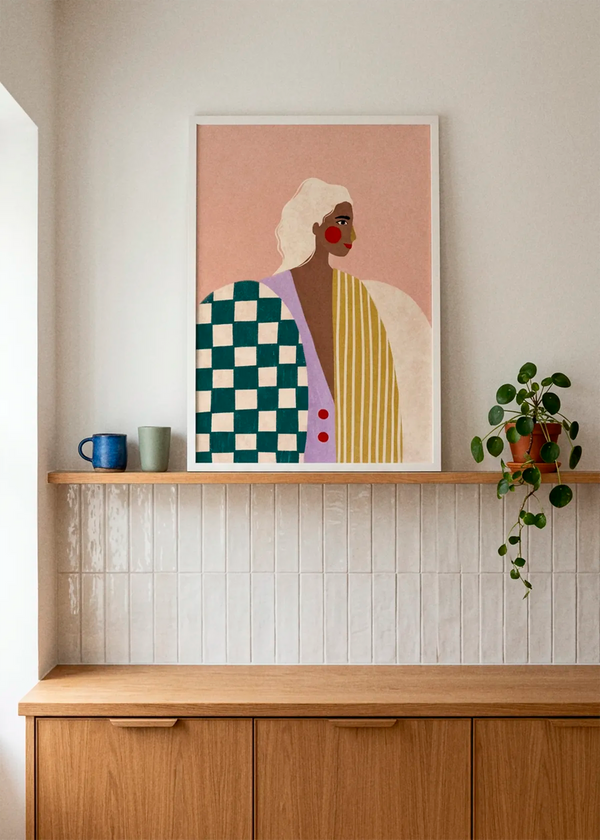Bold Fashion Portrait by Bea Müller displayed in a white frame above warm oak kitchen cabinetry, styled with ceramic cups, glossy white tiles and a soft neutral wall.