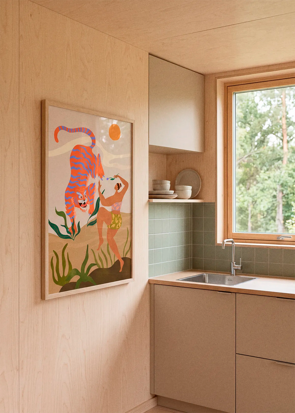 Dance With Me by Arty Guava art print featuring a woman dancing beside a vivid orange and blue tiger among tropical plants, displayed in a light wood frame in a warm Scandinavian kitchen.