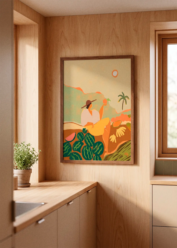 Farmer Guava by Arty Guava art print featuring a seated figure surrounded by watermelons, tropical fruit and a palm tree in warm green, yellow and orange tones, displayed in a dark wood frame in a warm Scandinavian kitchen.