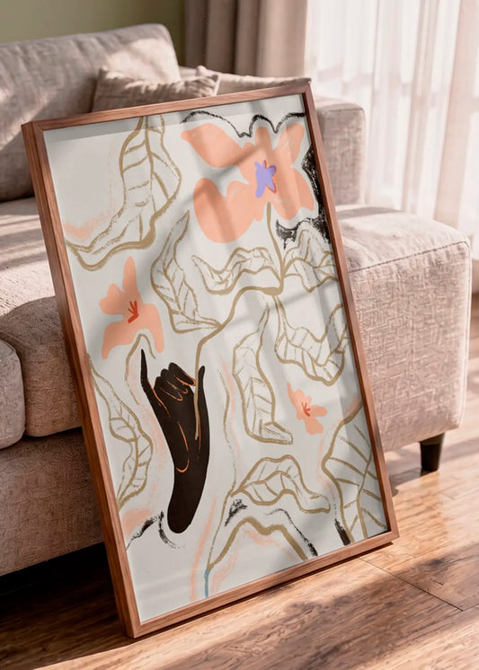 Indrammet kunstplakat med abstrakte blomster i rosa nuancer, placeret op ad en beige sofa i et lyst hjem.