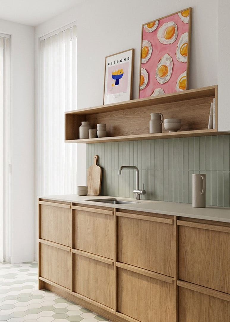 Kitchen wall art with fried egg poster and “Citrons” print in oak frames styled above wooden cabinets in bright Scandinavian kitchen.