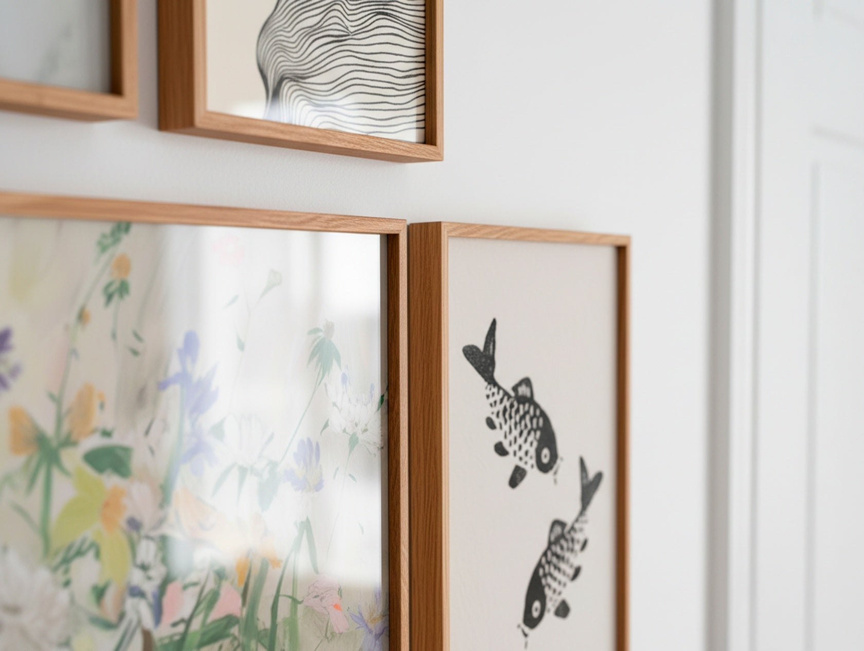 Close-up of oak frames featuring a floral poster and a black-and-white koi fish print on a light Scandinavian wall.