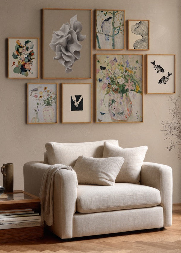 Styled gallery wall in a Scandinavian living room with a mix of botanical prints, abstract shapes, and delicate bird illustrations in oak frames above a beige armchair.