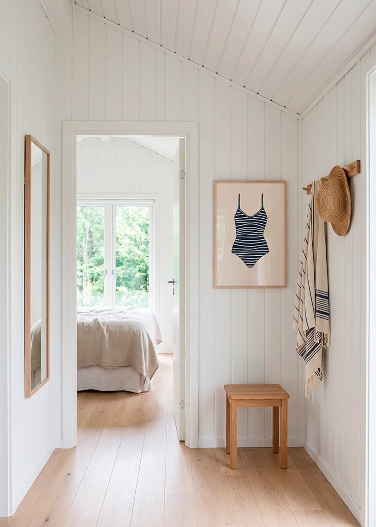 Striped swimsuit poster in oak frame styled in bright Scandinavian summer house hallway with wooden floor and natural light