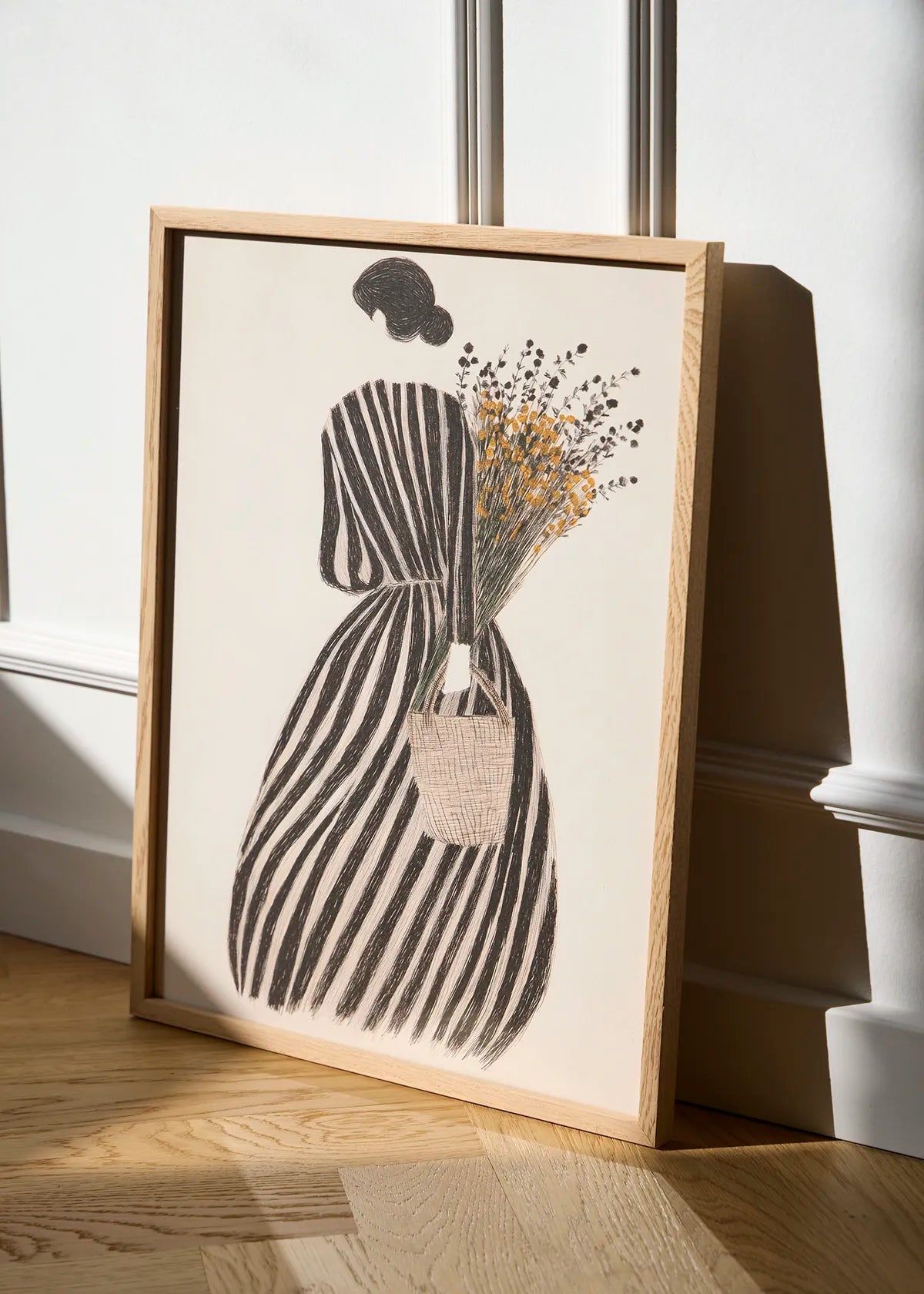 MariGold woman poster in an oak frame leaning against a white wall in natural sunlight, featuring black stripes and golden wildflowers.