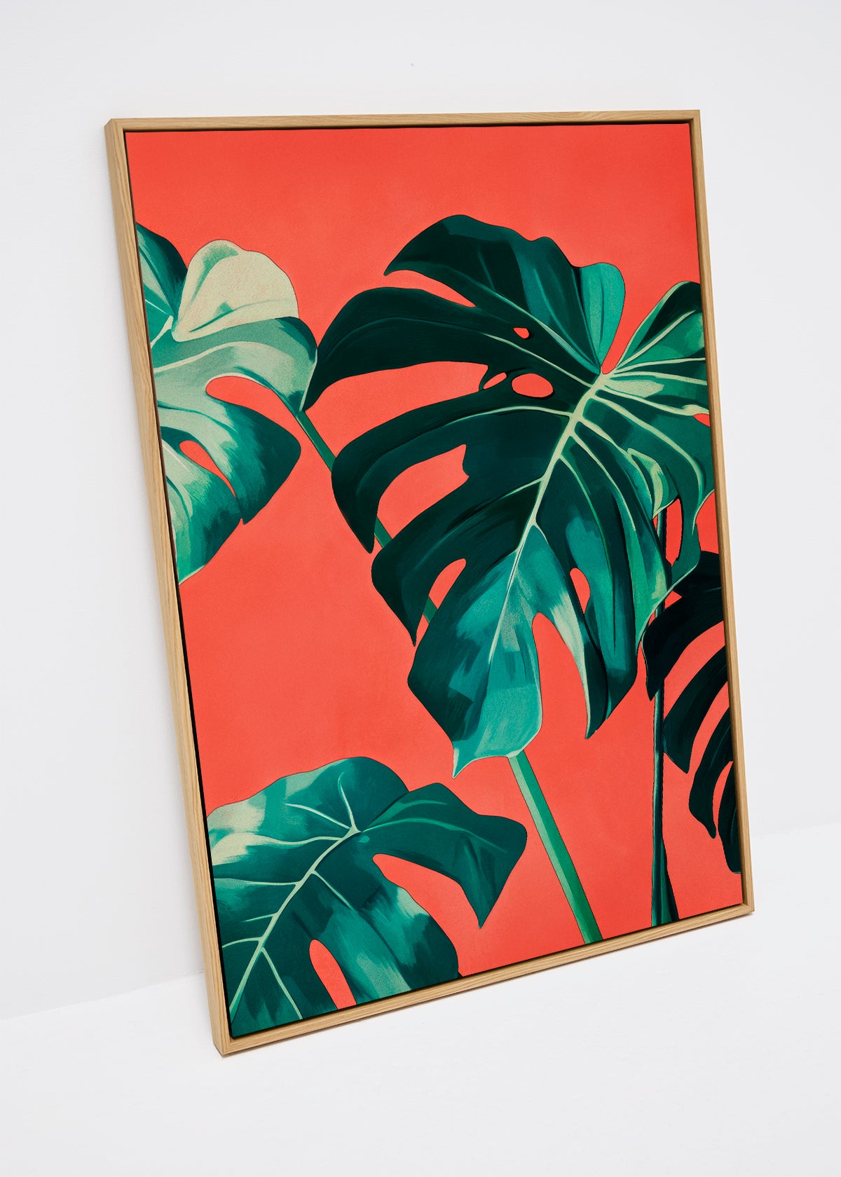 Canvas print of green monstera leaves on a coral background in wooden frame.