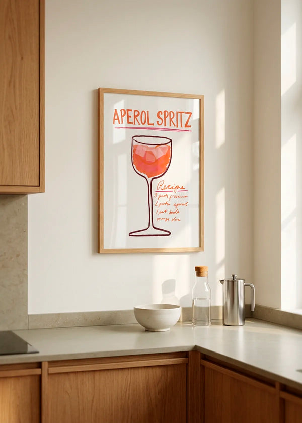 Recipe Delight by Athene Fritsch – framed Aperol Spritz recipe poster in orange and coral tones, styled in a bright warm kitchen with natural wood cabinetry.
