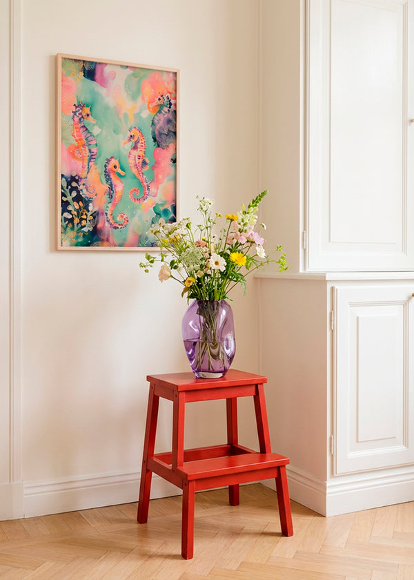 Sea World poster with colourful seahorses displayed in a bright Scandinavian interior, styled above a red wooden stool with a glass vase of fresh flowers, creating a calm and playful atmosphere.