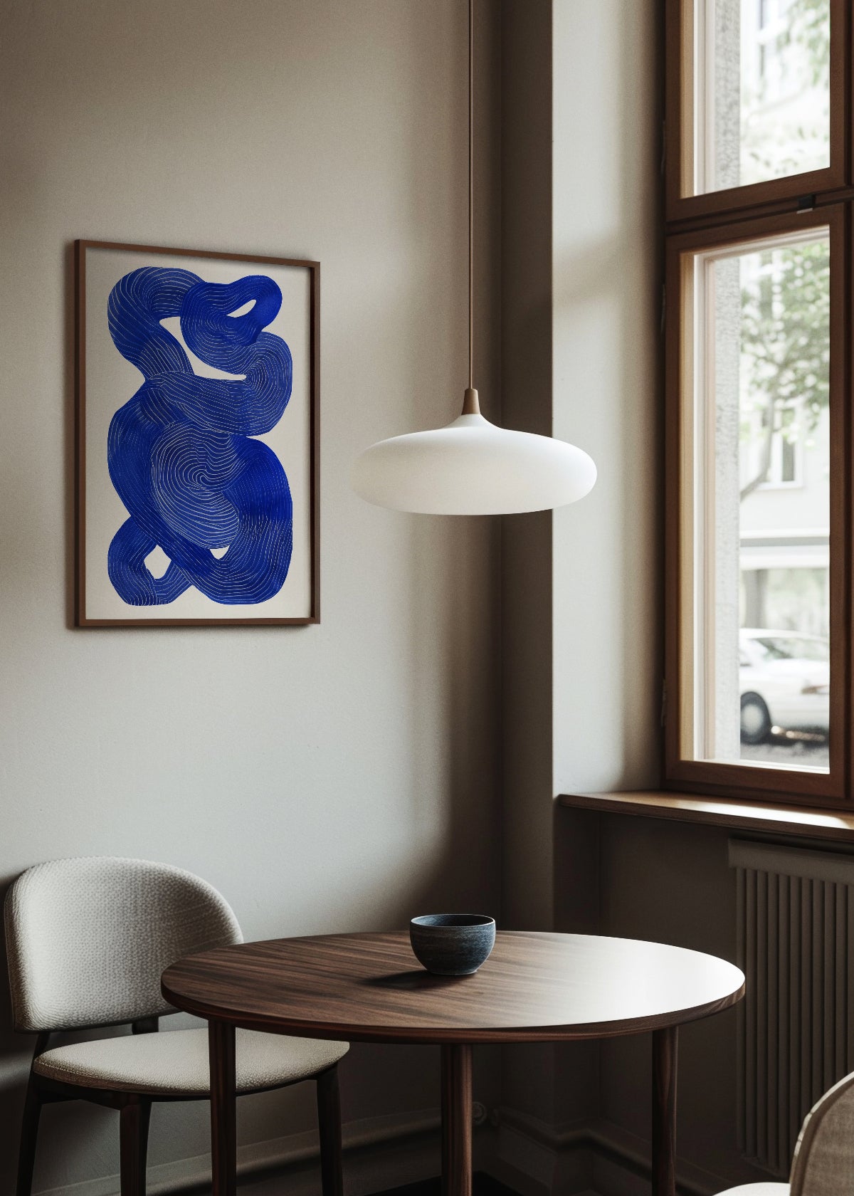 Framed poster 'Shape no. 10' in a cozy dining nook with soft lighting and minimalist decor. The artwork features an abstract blue form with swirling line details on a neutral background.
