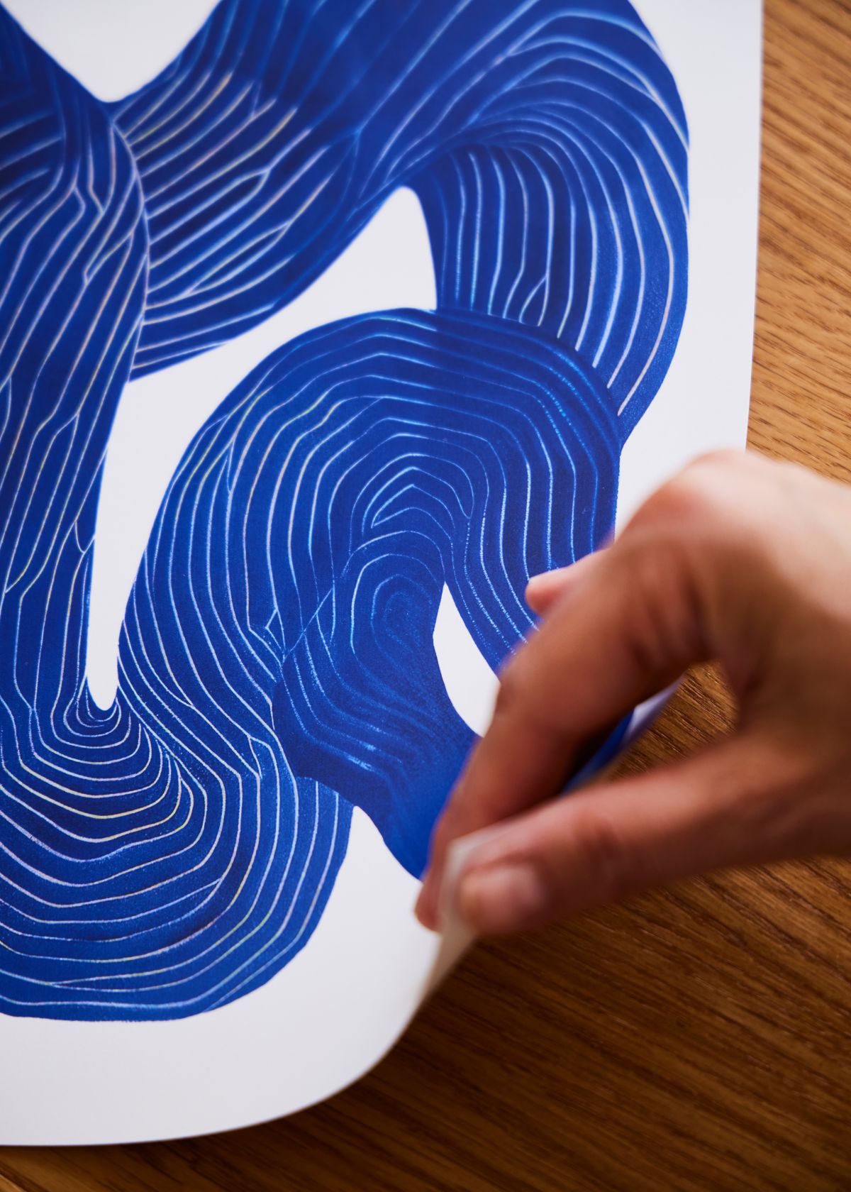Hånd der holder hjørnet af Shape No. 10 plakat, som viser den blå abstrakte linjekunst på FSC-certificeret papir med mat overflade.