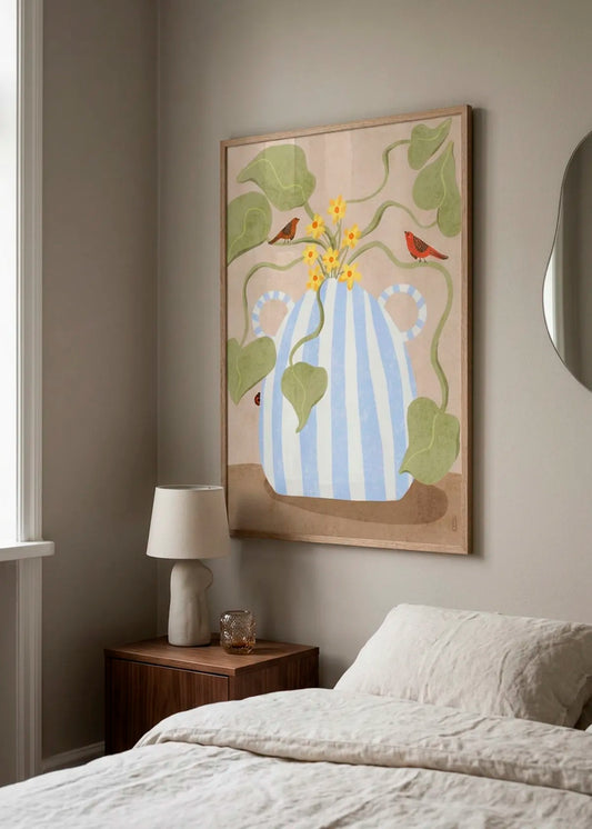 Spring Flowers and Birds by Dirkie Nell – framed art poster with a blue and white striped vase, yellow flowers, green leaves and two red birds, styled in a calm neutral bedroom interior.