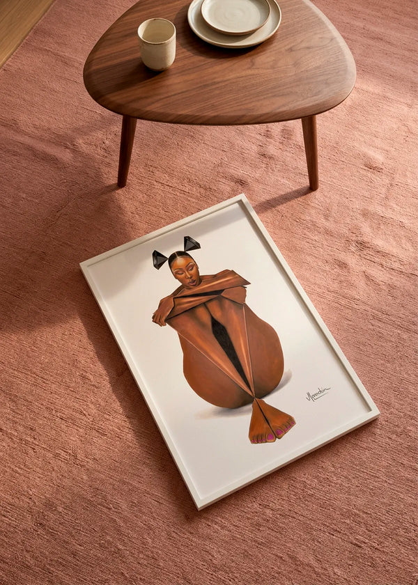 Thoughtful Folded Woman by Manasseh Johnson Sr. art print featuring a seated woman in a sculptural folded pose, displayed in a white frame on a dusty rose rug beside a wooden coffee table.