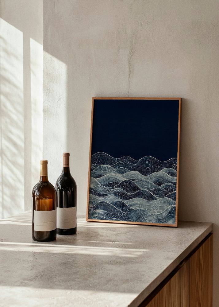 Tide poster showcasing elegant waves in shades of blue on a deep navy background. The artwork is framed in natural wood and placed on a modern concrete countertop next to two minimalist wine bottles, creating a serene and stylish ambiance.