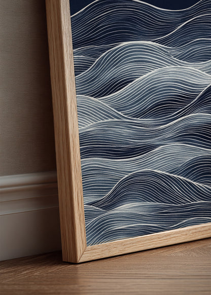 Minimalist blue and white abstract wave print in light oak frame, leaning against a beige wall in a modern, calm home interior.