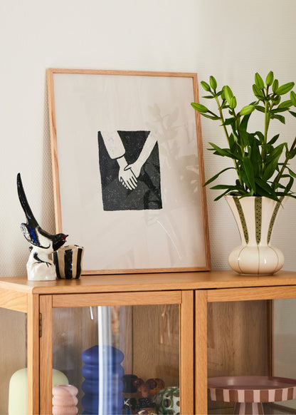 Togetherness poster in dark wooden frame placed on a cabinet, decorated with books, flowers, and artistic objects in a cozy home setting.