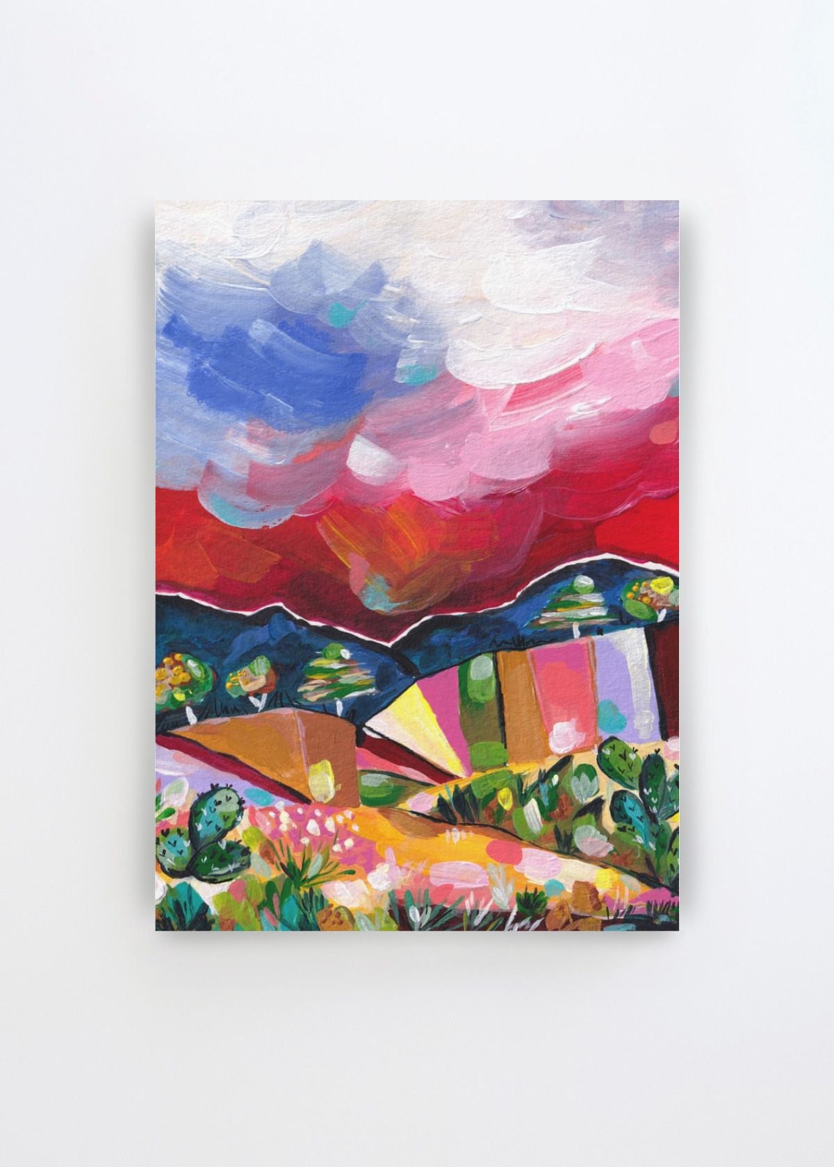 Vibrant Desert Landscape by Dirkie Nell art print featuring an expressive desert scene with colourful mountains, cacti and desert plants beneath a dramatic pink, red, blue and white sky.