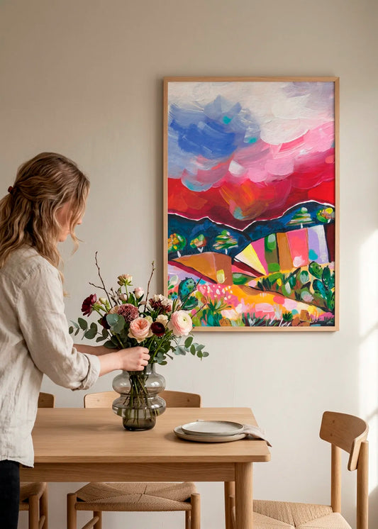Vibrant Desert Landscape by Dirkie Nell – framed colourful desert landscape art poster with pink, red, blue and green tones, styled above a wooden dining table in a bright warm interior.