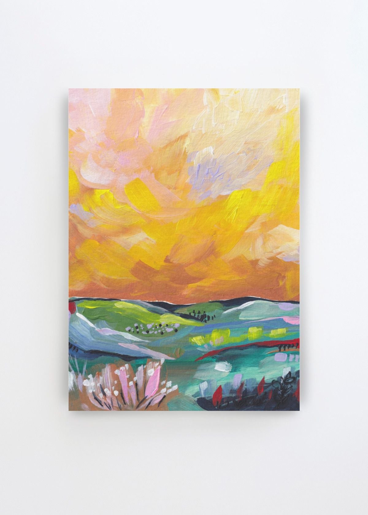 Vibrant Sunset Landscape by Dirkie Nell art print featuring rolling green and blue hills beneath an expressive sunset sky in yellow, peach, pink and soft lavender tones, with colourful flowers and plants in the foreground.