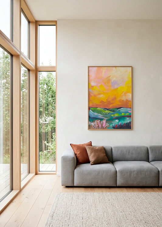 Vibrant Sunset Landscape by Dirkie Nell – framed colourful landscape art poster with golden sunset tones, green hills and blue water, styled above a grey sofa in a bright modern living room.