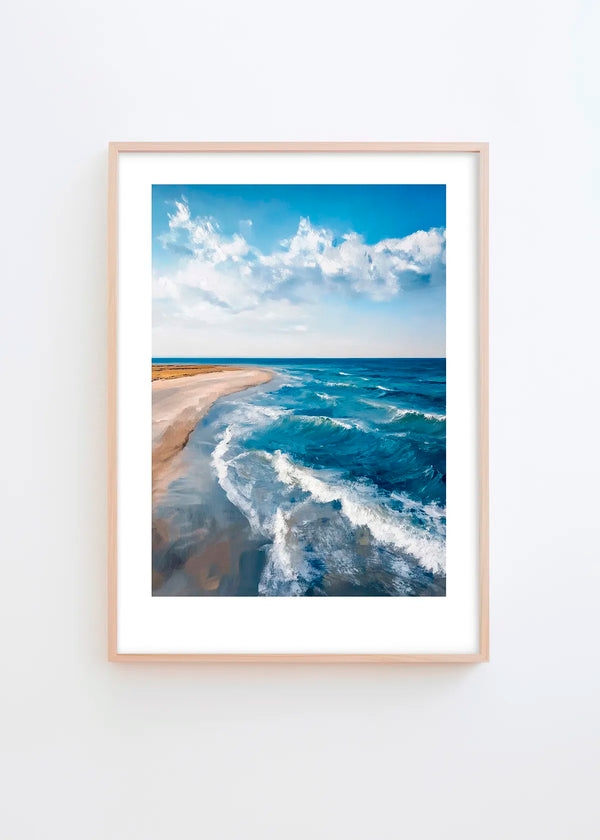 Where the Sea Meets poster in a minimalist Scandinavian interior with light grey wall and natural wood frame, featuring blue ocean waves, sandy beach and soft sky tones.