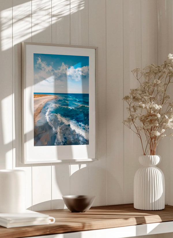 Where the Sea Meets poster in a bright Scandinavian room with wooden surface and neutral decor, featuring coastal waves, sandy shoreline and calming blue ocean tones.