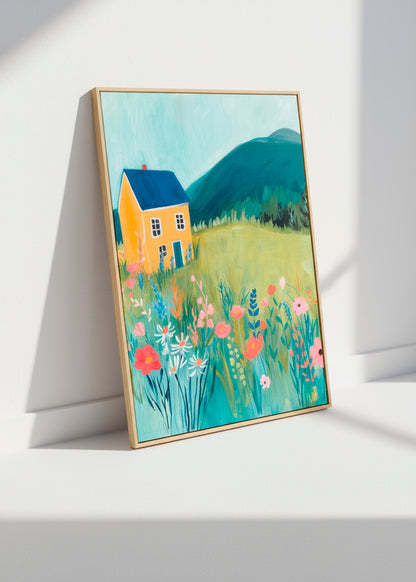 Framed Yellow House canvas leaning against a white wall in soft sunlight, showing a meadow full of colorful flowers.