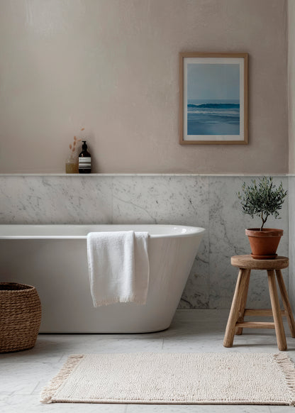 Soothing ocean-themed poster titled "Calm" in a light wood frame, hanging above a white bathtub in a serene, Scandinavian-style bathroom.