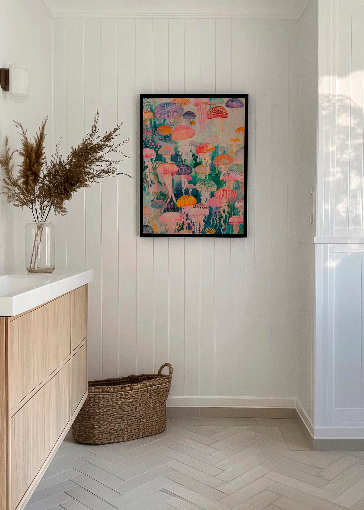 Minimalist bathroom featuring the "Under Water" poster, showcasing colorful jellyfish in soft pastel tones. The artwork is framed in black and displayed on a white paneled wall. Decorative elements like dried branches in a glass vase and a woven basket on the floor add a natural and calming touch.